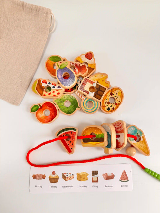 Colorful wooden food pieces and a caterpillar threading toy with weekly menu cards on a white background.