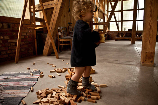 Toddler playing with natural wooden blocks on the floor, showcasing creativity and imaginative play.