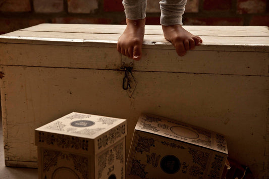 Child's feet on a wooden chest with decorative boxes nearby, capturing playful exploration and creativity.