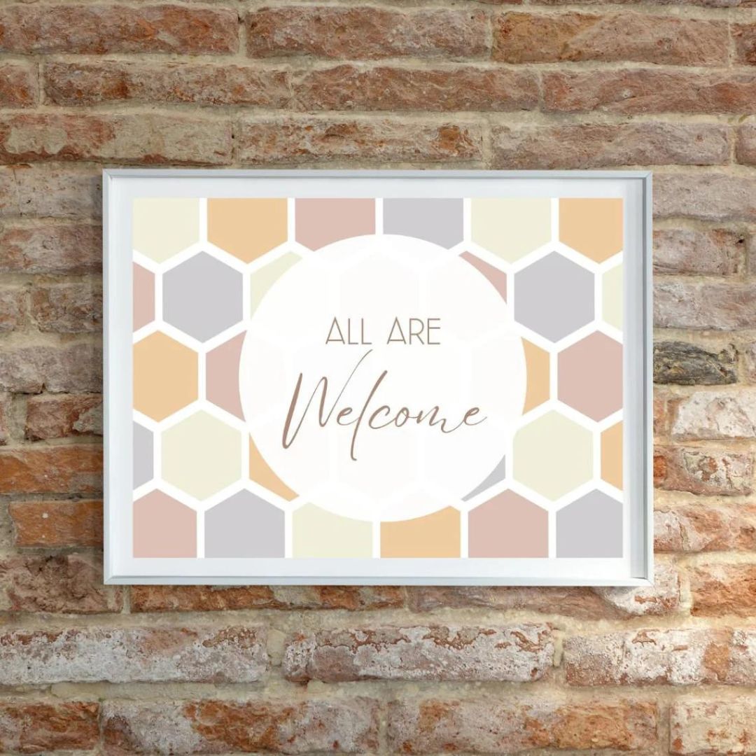 Framed poster on brick wall with pastel honeycomb design, featuring the text 'All Are Welcome' in elegant script.