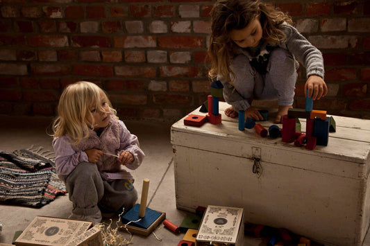 Two children engaging creatively with wooden rainbow building blocks on a rustic wooden trunk.