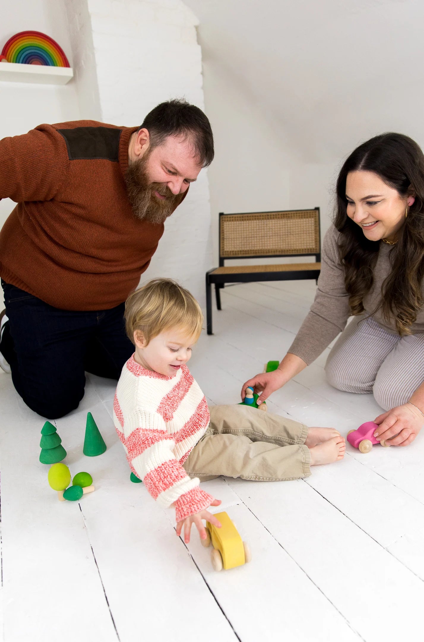 A family playing with colorful wooden toys on a white floor, engaging in fun and creative activities.