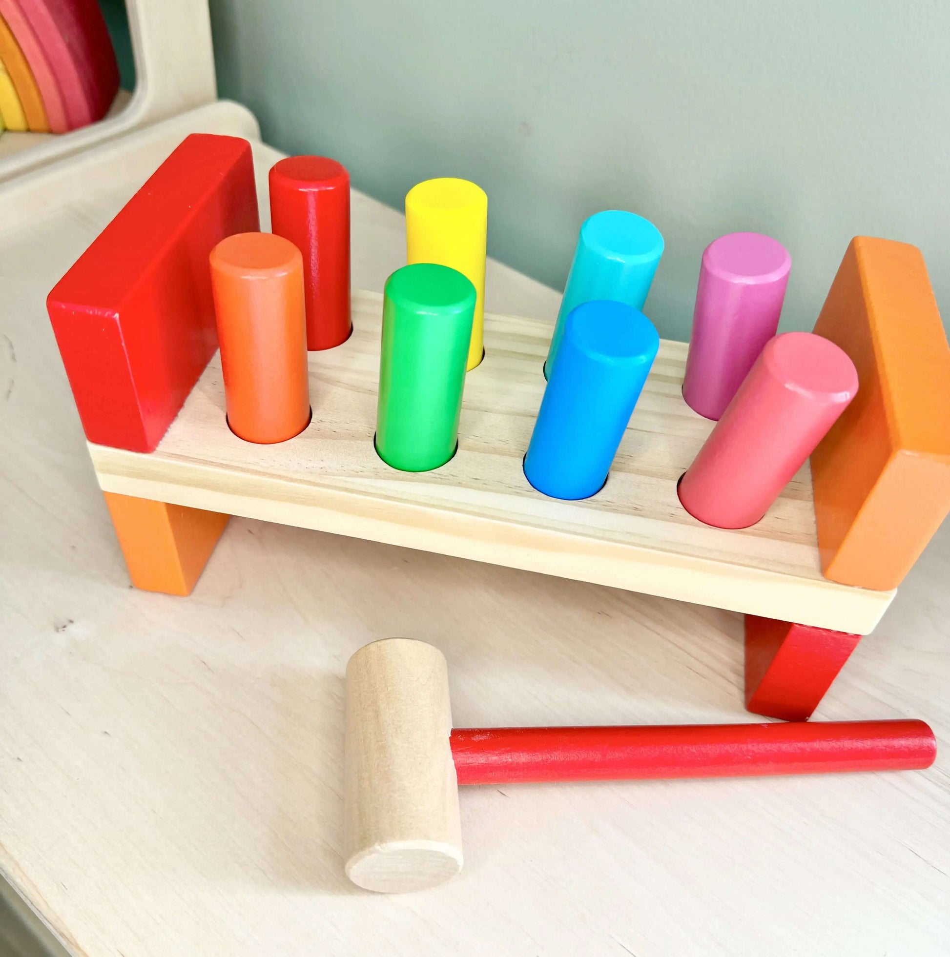 Vibrant wooden peg bench and hammer set for toddlers promoting Montessori-inspired open-ended play and fine motor skills.