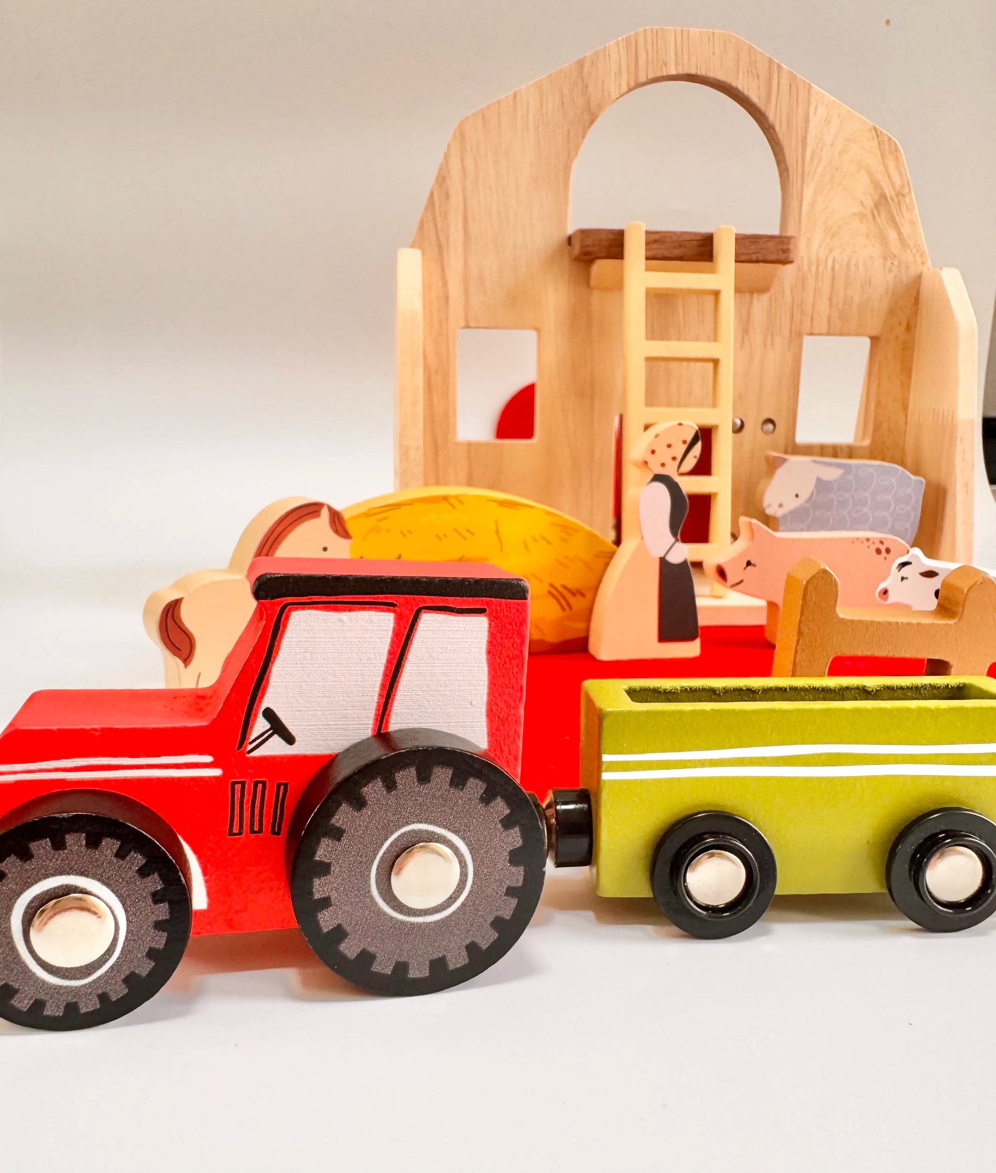 Colorful wooden tractor and farm figures in front of a folding wooden farmyard house for imaginative play.