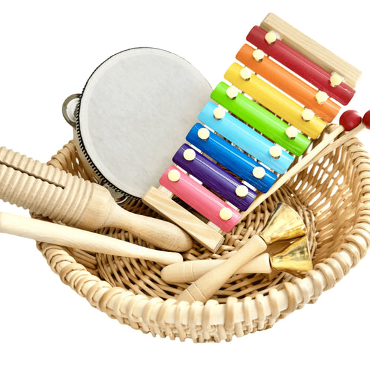 Basket of wooden musical instruments including a xylophone, tambourine, and percussion tools for open-ended, Montessori-inspired play