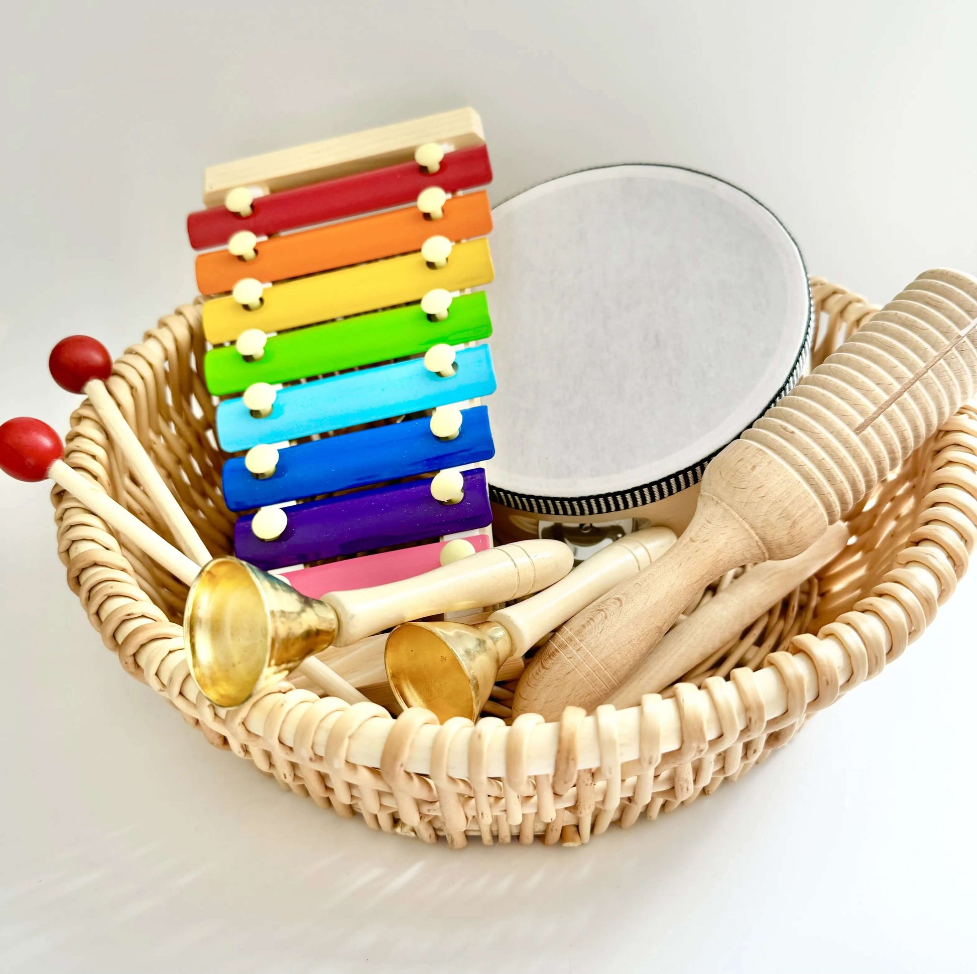 Basket of colorful wooden musical instruments for babies including xylophone and tambourine, Montessori-inspired eco-friendly toy.