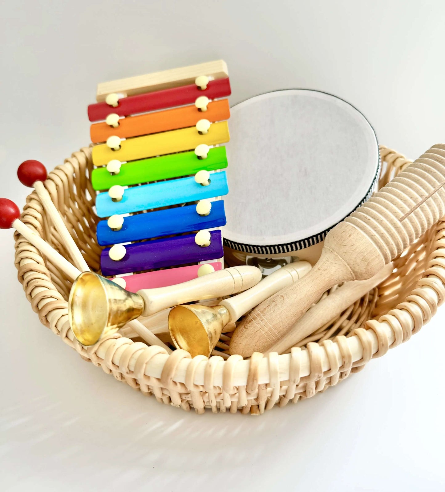 Basket of assorted wooden musical toys including xylophone, tambourine, and bells for Montessori-inspired open-ended sensory play.