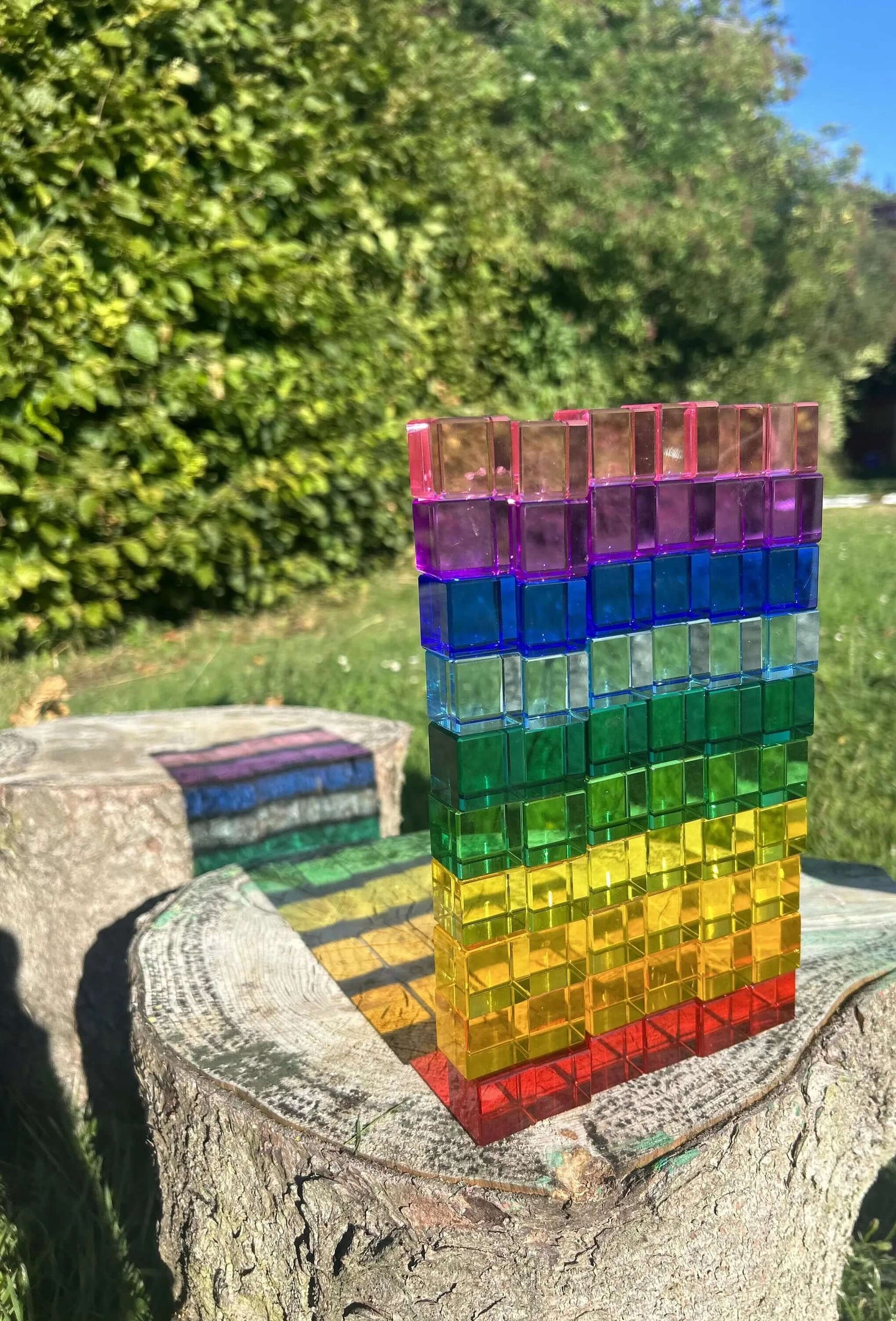 Colorful acrylic Permeability Cubes arranged on a tree stump, promoting open-ended, Montessori inspired educational play outdoors.