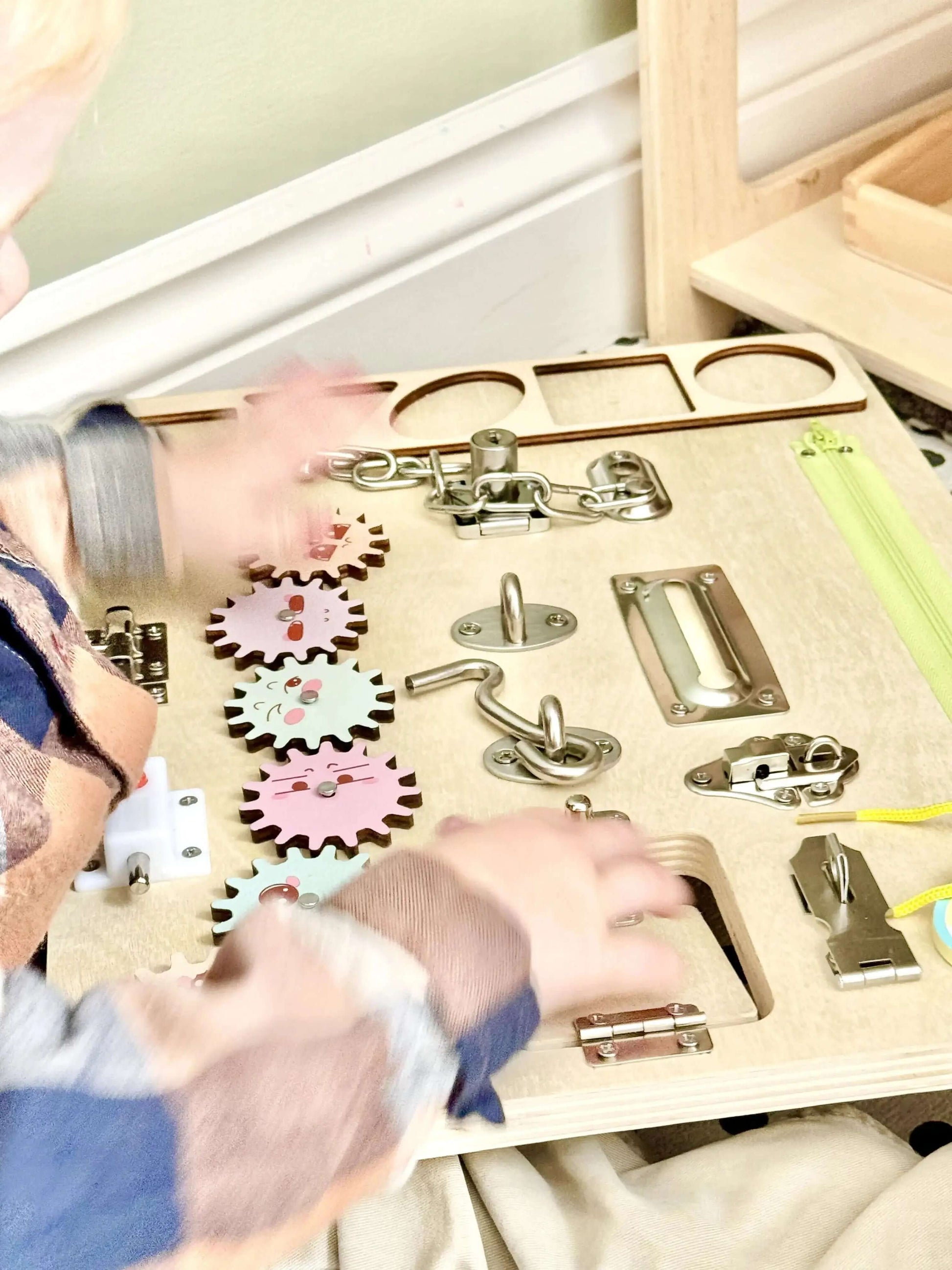 Child playing with Montessori inspired wooden busy board featuring latches, gears, and other engaging elements for open-ended play.