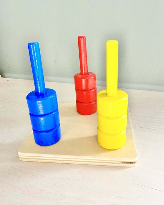 Wooden Montessori toy with red, yellow, and blue coloured dowels and rings for open-ended play, boosting fine motor skills and hand-eye coordination.