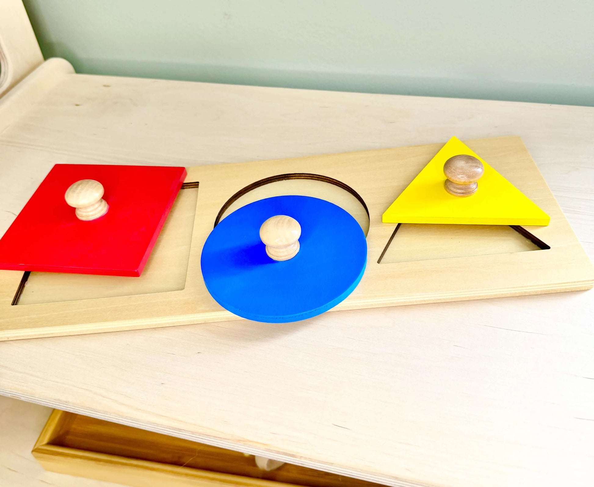 Wooden Montessori puzzle toy with red square, blue circle, and yellow triangle shapes, ideal for open-ended, eco-friendly play.