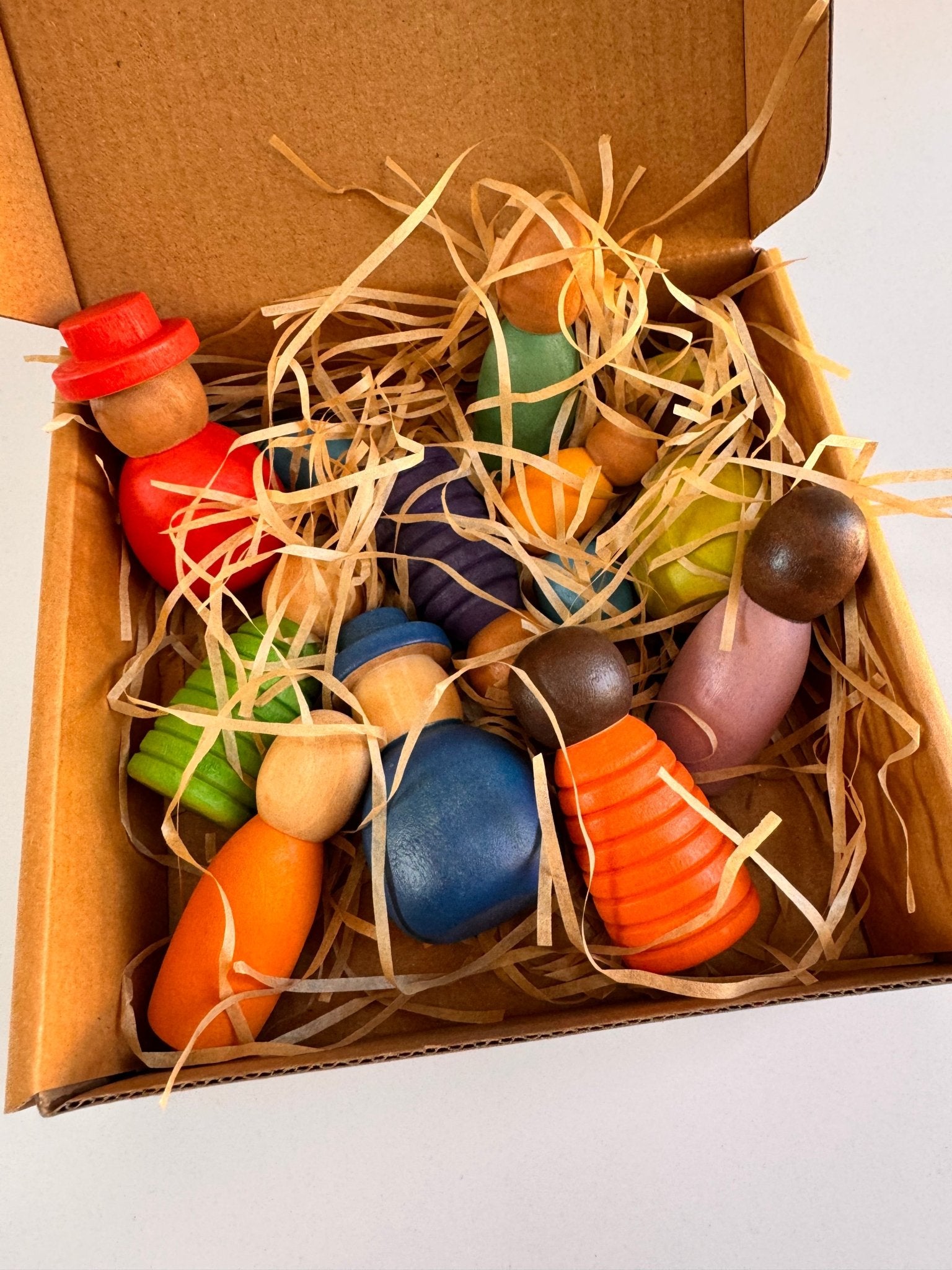 Colorful wooden peg dolls in a box with straw, celebrating diversity and imaginative play.