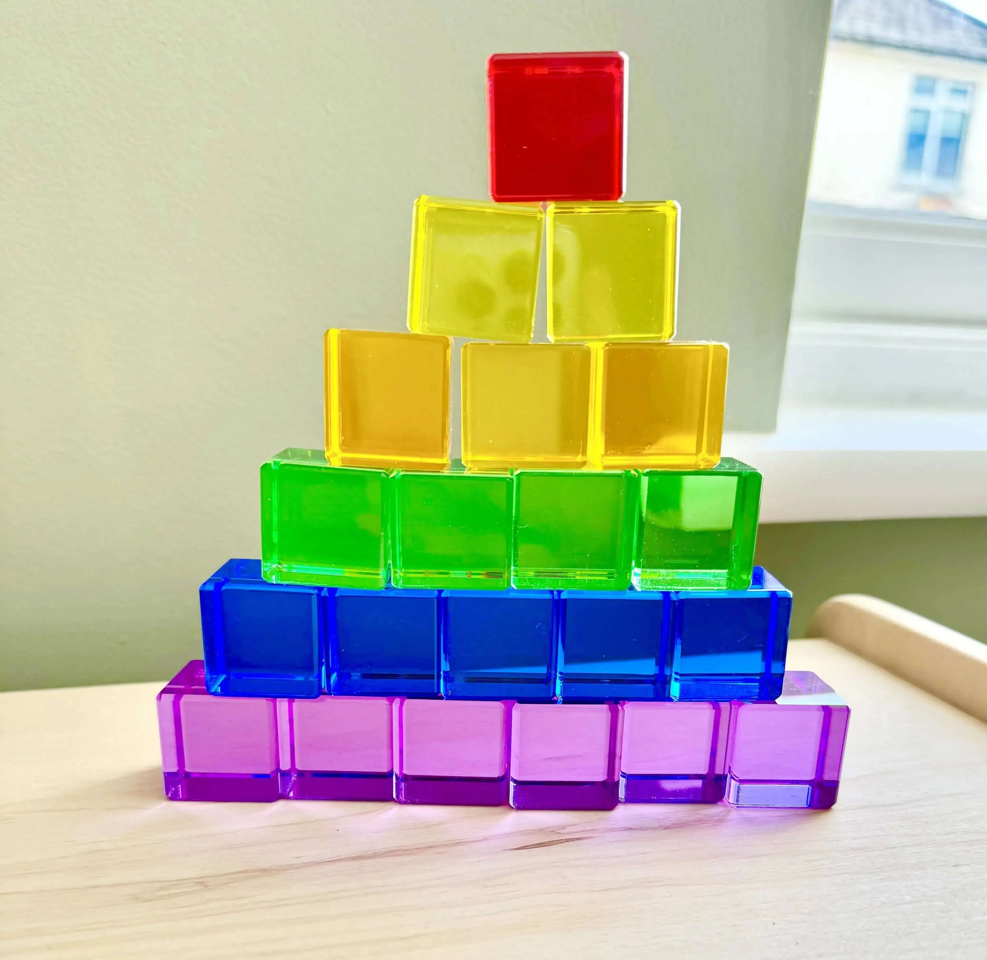 Acrylic Permeability Cubes stacked in a colorful pyramid for Montessori-inspired open-ended play on a wooden toy table.