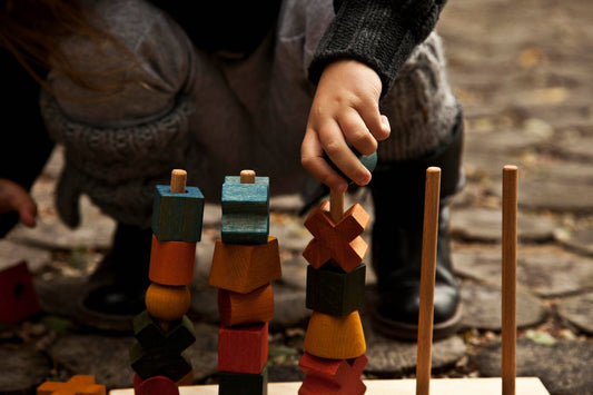 Child stacking colorful wooden shapes with a playful focus on creativity and sensory exploration.