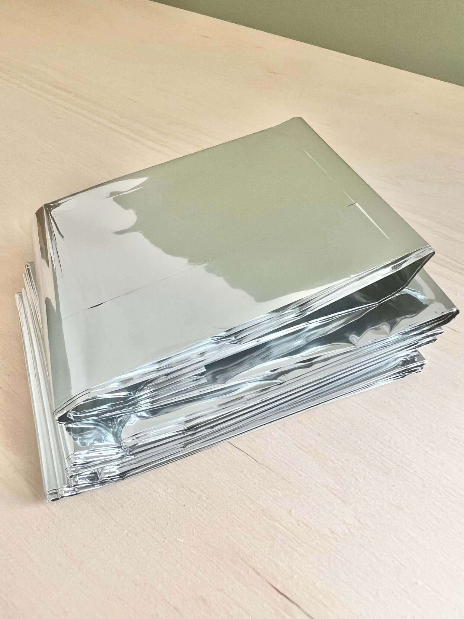 Stack of shiny silver mylar bags on a light wooden surface.