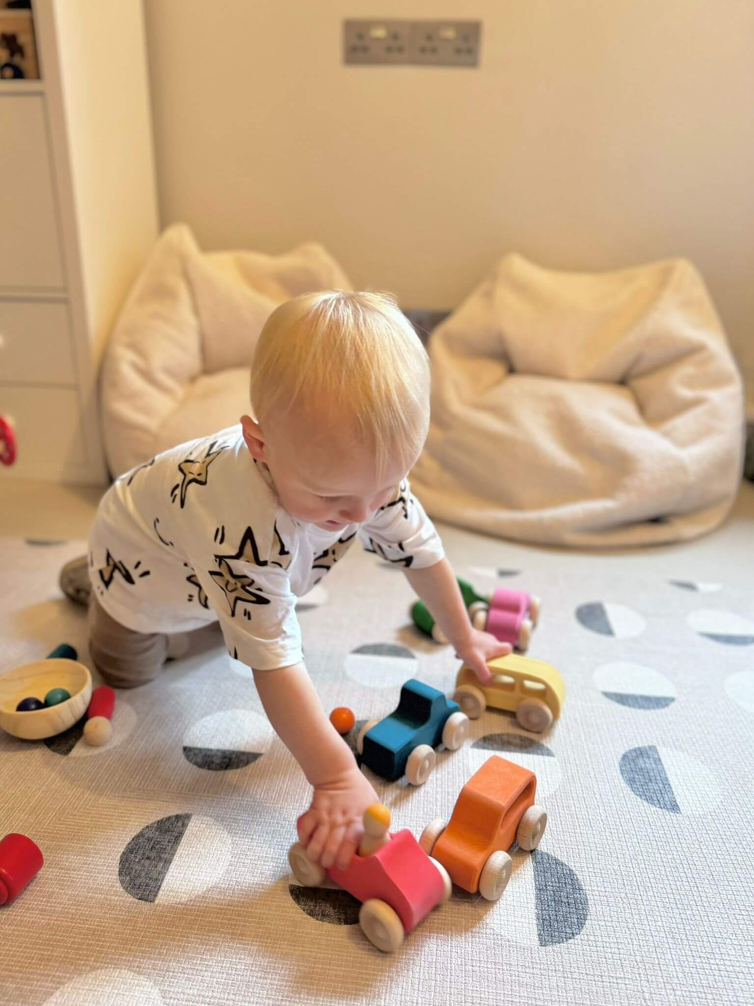 Toddler playing with Rainbow Wooden Cars set on a carpet, showing sustainable Montessori toys made from non-toxic materials.