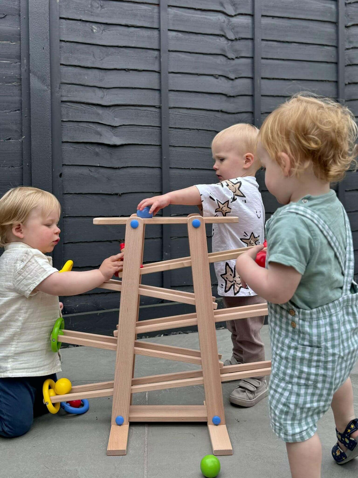 Toddlers engaging with a wooden shape ramp, a Montessori-inspired toy promoting open-ended play, hand-eye coordination, and problem-solving skills.