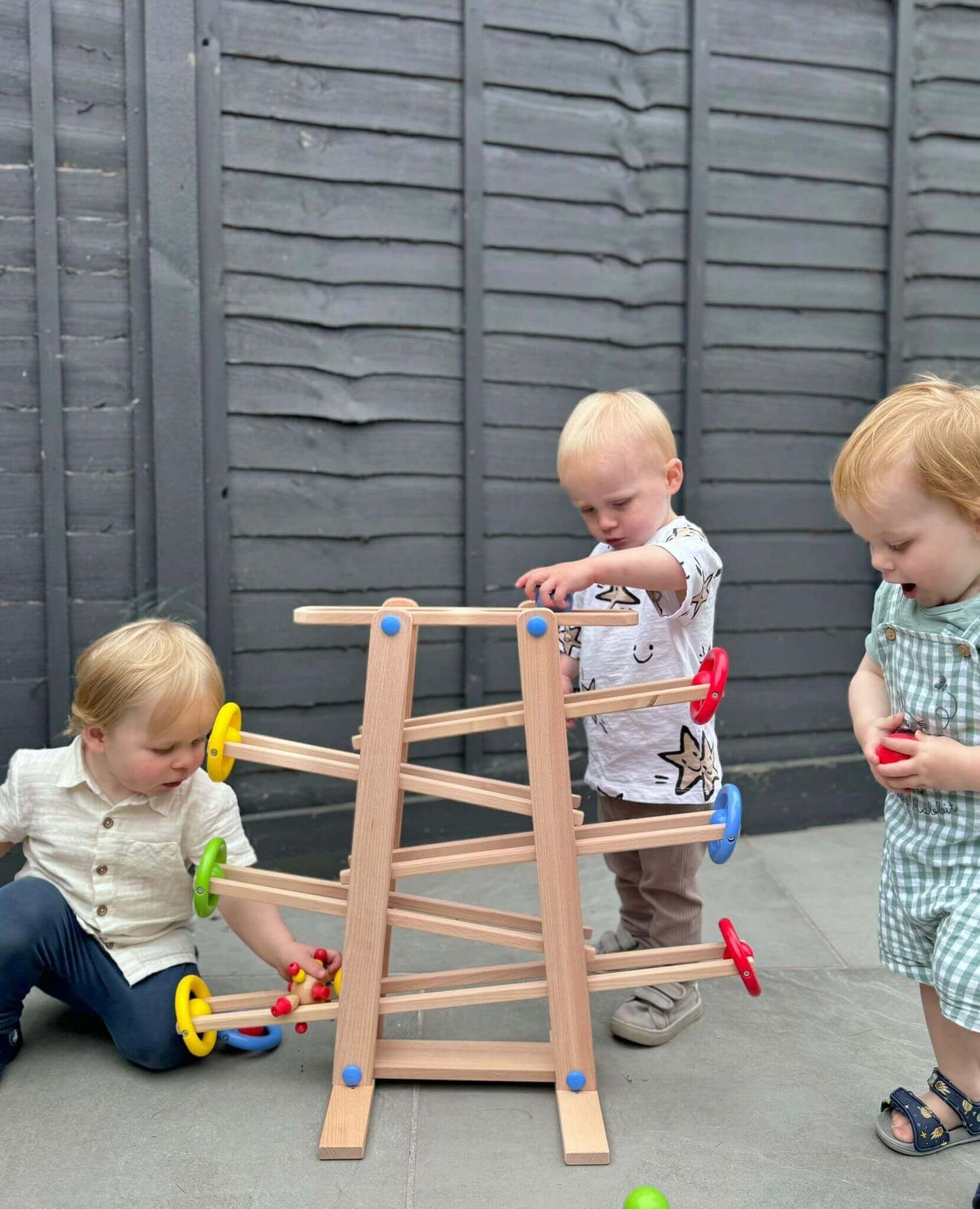 Toddlers playing with a Montessori inspired wooden shape ramp, engaging in open-ended play and developing problem-solving skills.